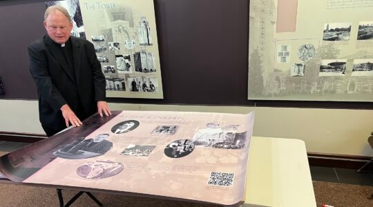 A priest stands over a poster about to be mounted on a wall