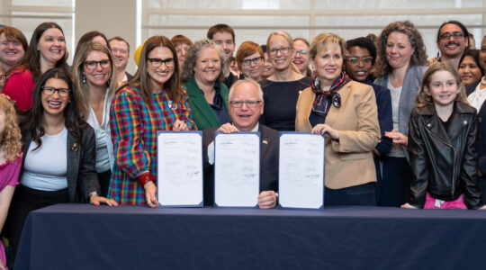 A governor smiles in front of three signed bills with smiling women and men behind him